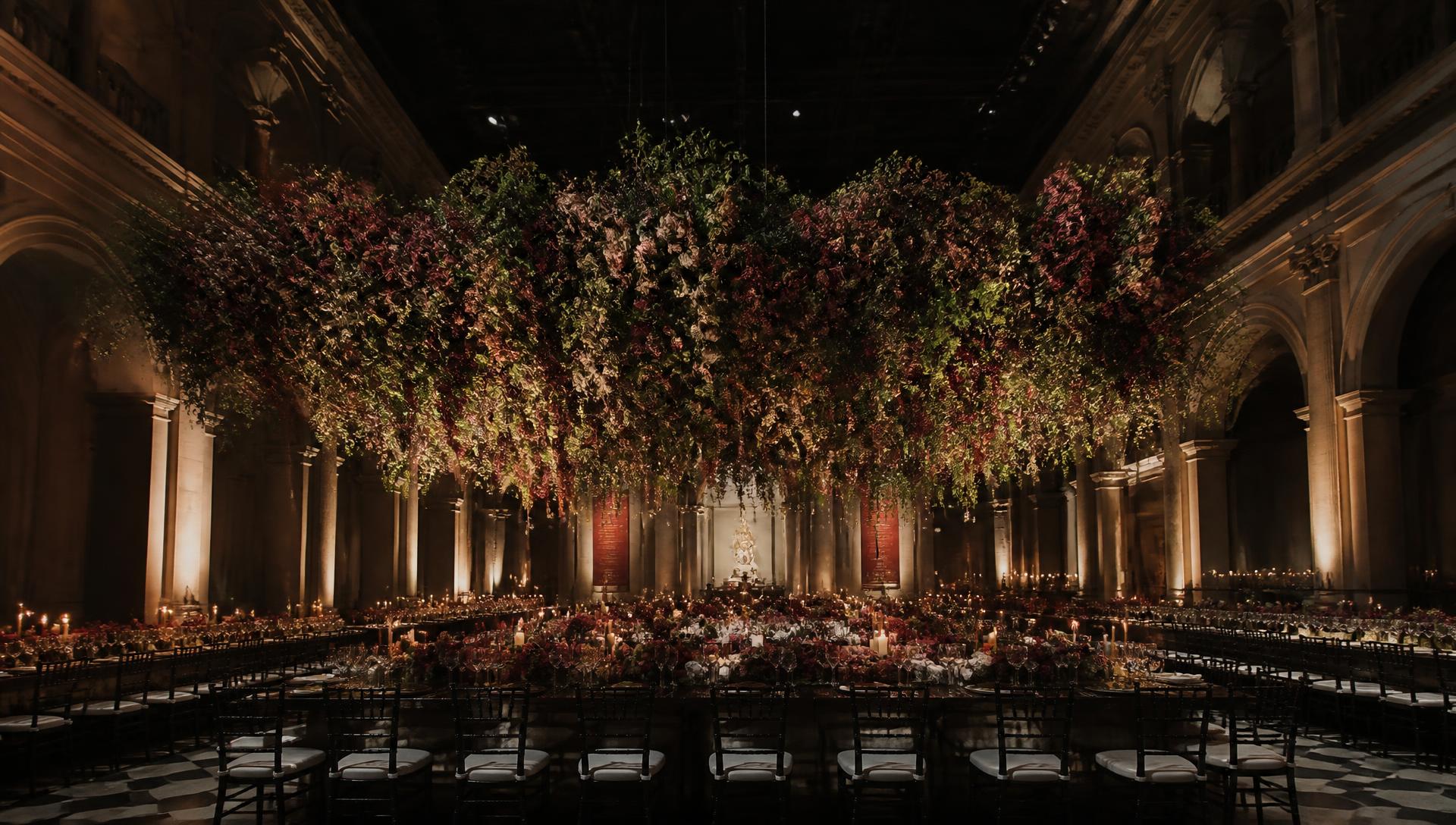 Gala dinner hall with a suspended floral installation above long candlelit tables